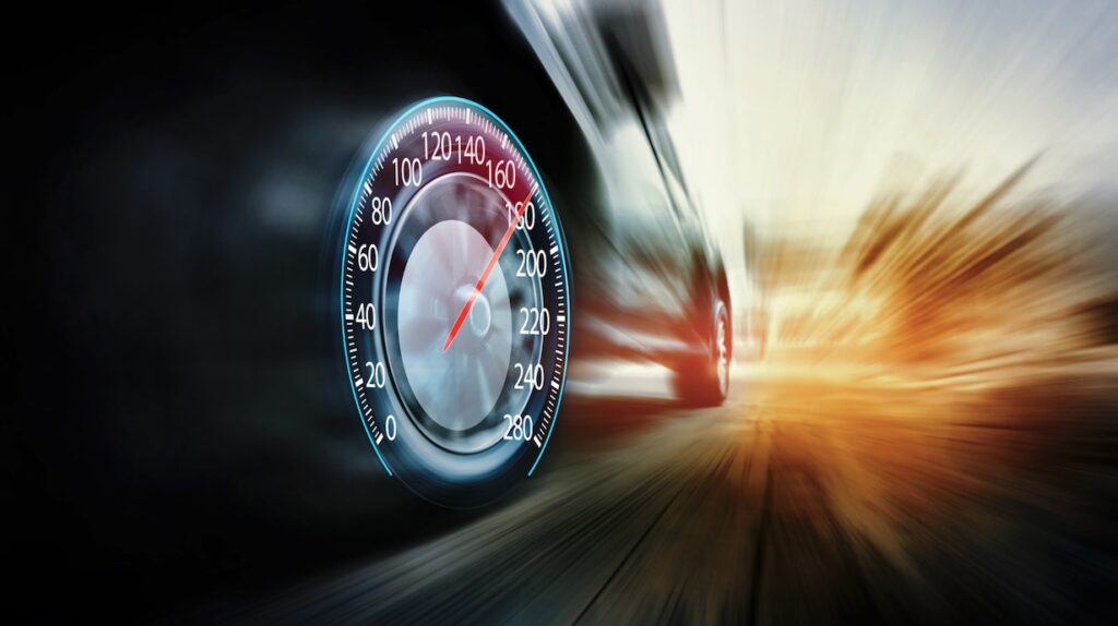 A car wheel replaced by a speedometer showing a vehicle racing down the road.
